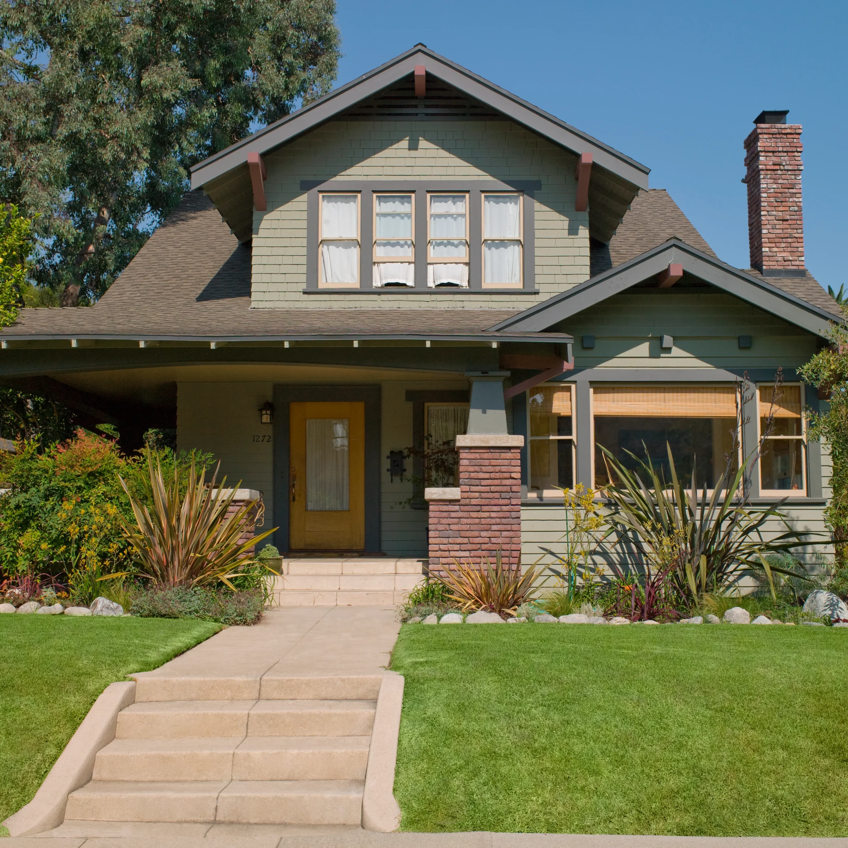 A charming Craftsman-style house with a well-maintained lawn and clear sky.