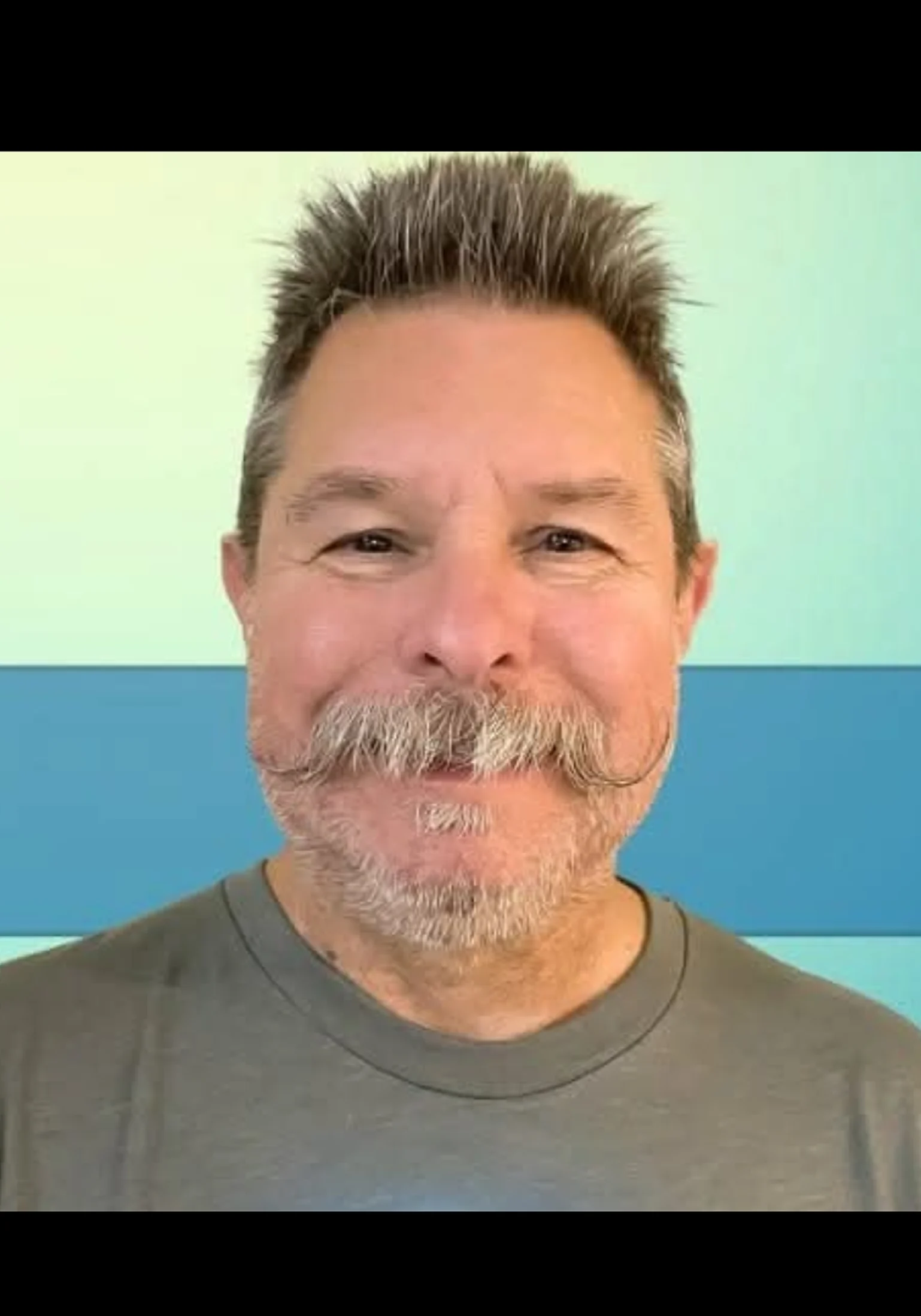 Smiling man with a mustache and short hair against a blue background.
